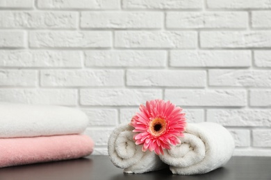 Photo of Rolled and folded soft towels with flower on table near brick wall. Space for text