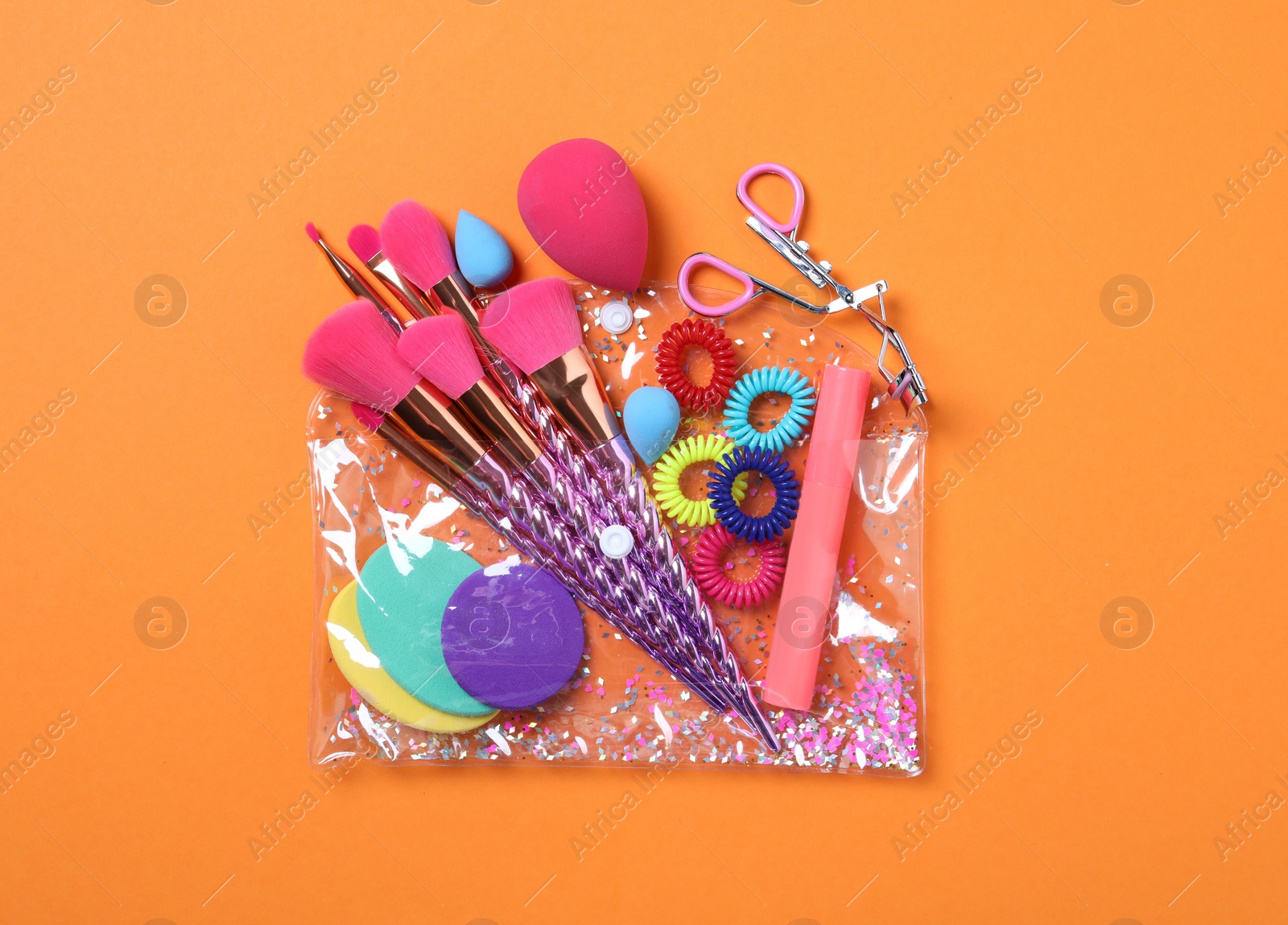 Photo of Plastic cosmetic bag with makeup products and beauty accessories on orange background, flat lay