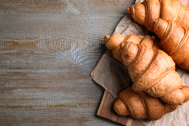 Photo of Tasty fresh croissants on wooden table, top view. Space for text