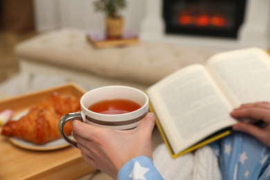 Photo of Woman with cup of tea and book resting at home, closeup