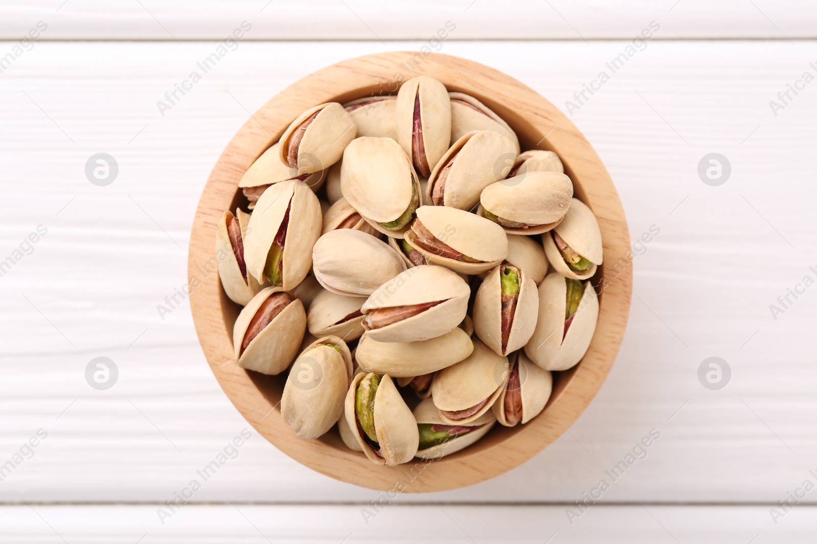 Photo of Tasty pistachios in bowl on white wooden table, top view