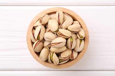 Tasty pistachios in bowl on white wooden table, top view