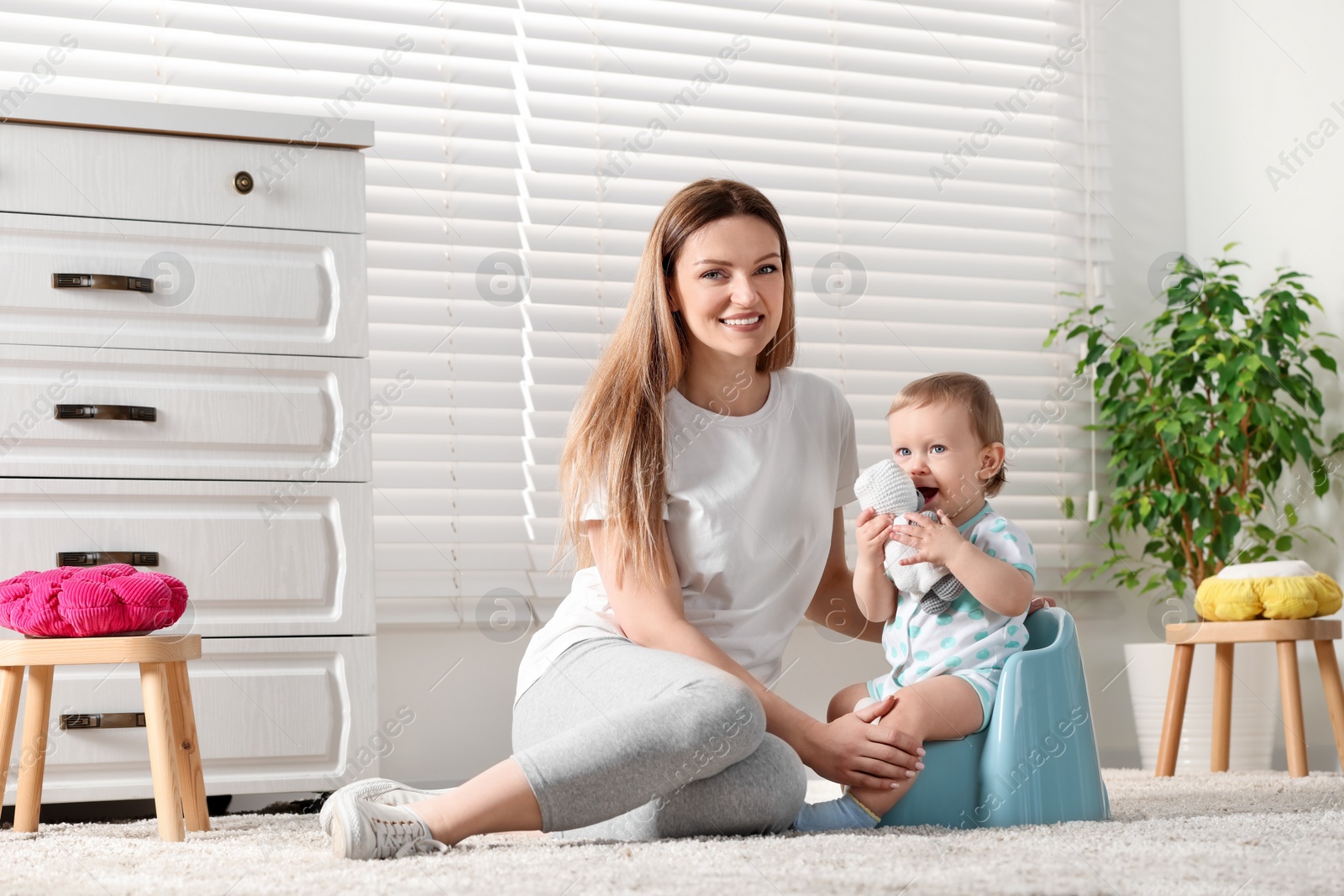 Photo of Mother training her child to sit on baby potty indoors