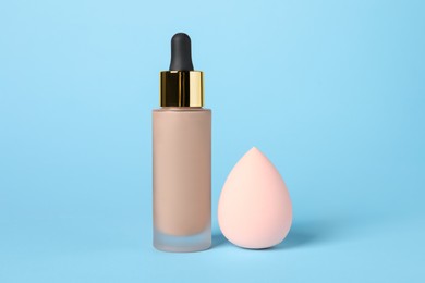 Photo of Bottle of skin foundation and sponge on light blue background. Makeup product