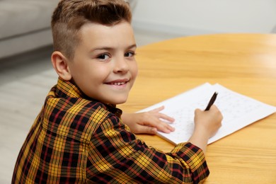 Little boy solving sudoku puzzle at table indoors