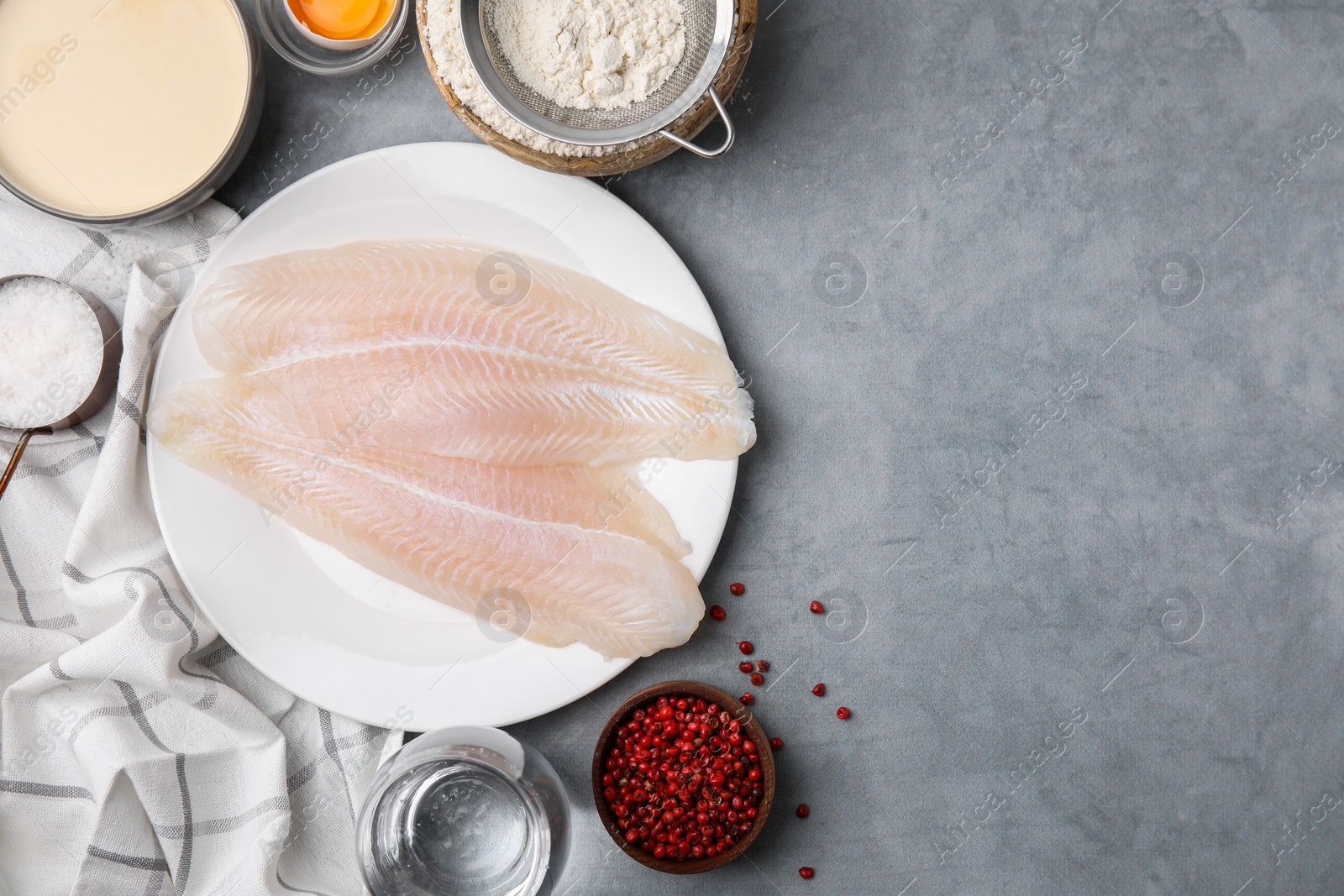 Photo of Different ingredients for soda water batter and raw fish fillet on grey table, flat lay. Space for text