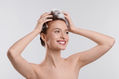 Photo of Happy young woman washing her hair with shampoo on light grey background