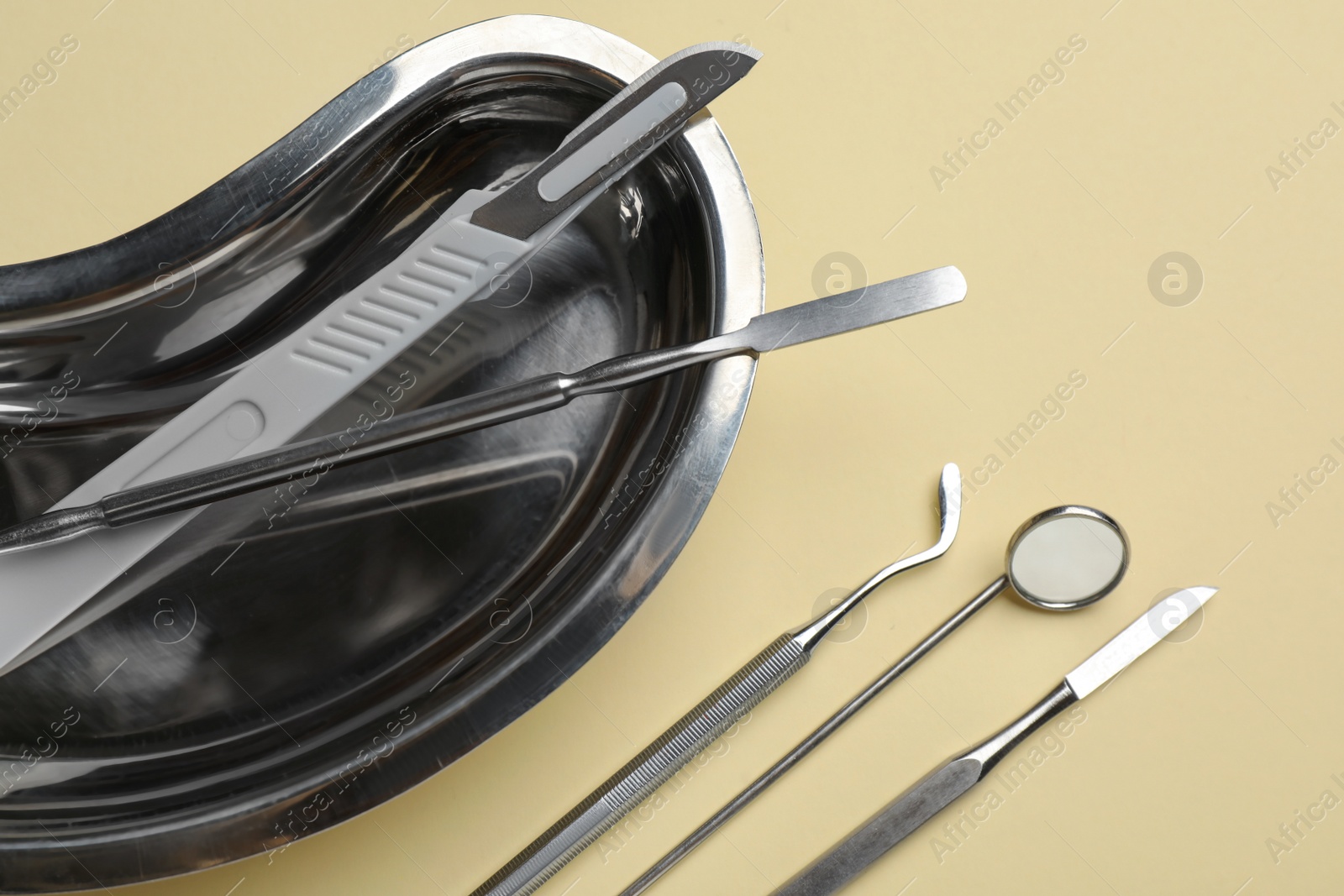 Photo of Kidney shaped tray with set of dentist's tools on pale yellow background, flat lay