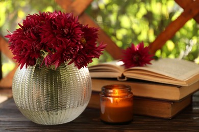 Beautiful pink chrysanthemum flowers, burning candle and books on wooden table