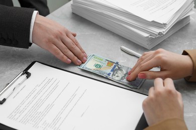 Woman giving money to man at light grey table, closeup