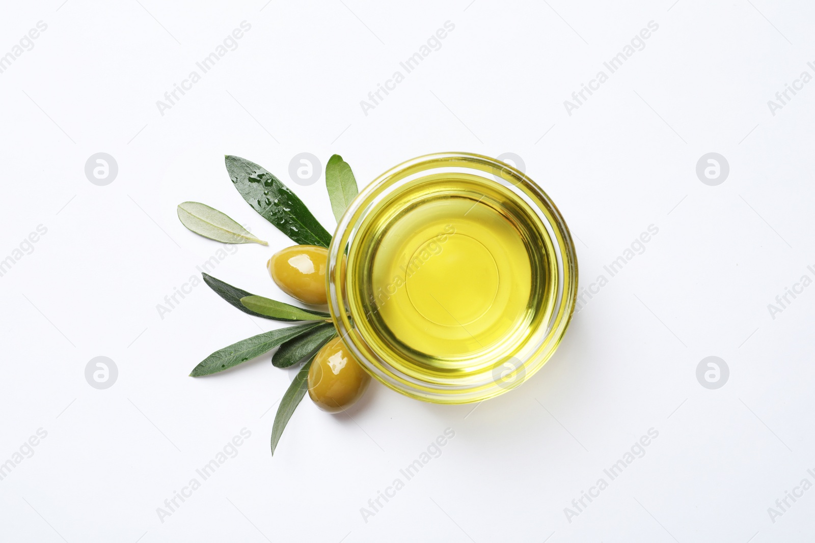 Photo of Little bowl with oil, ripe olives and leaves on white background