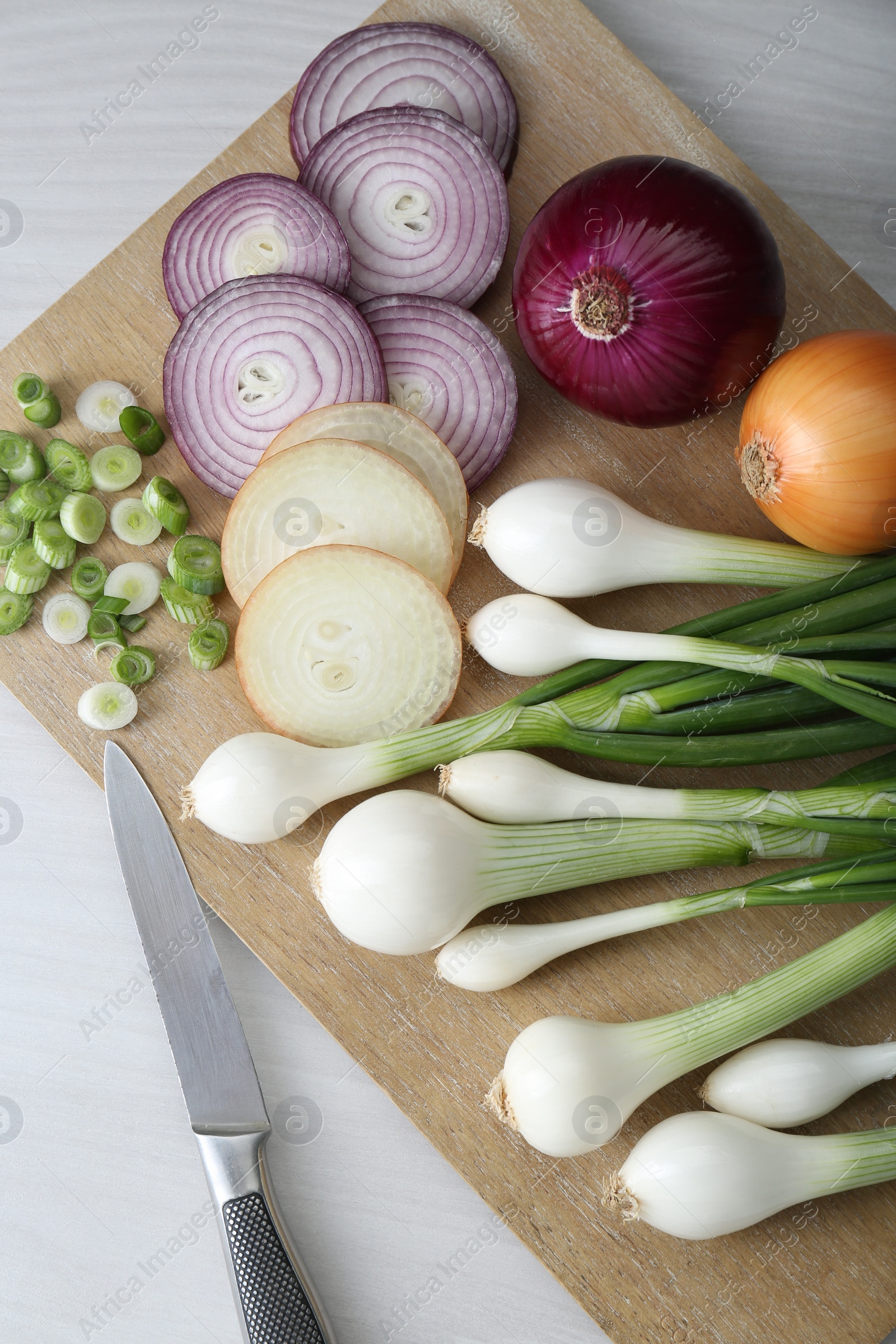 Photo of Board with different kinds of onions on white wooden table, top view