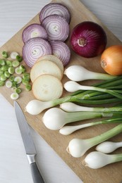 Board with different kinds of onions on white wooden table, top view