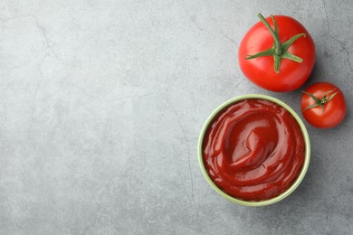 Photo of Bowl of tasty ketchup and tomatoes on light grey table, flat lay. Space for text