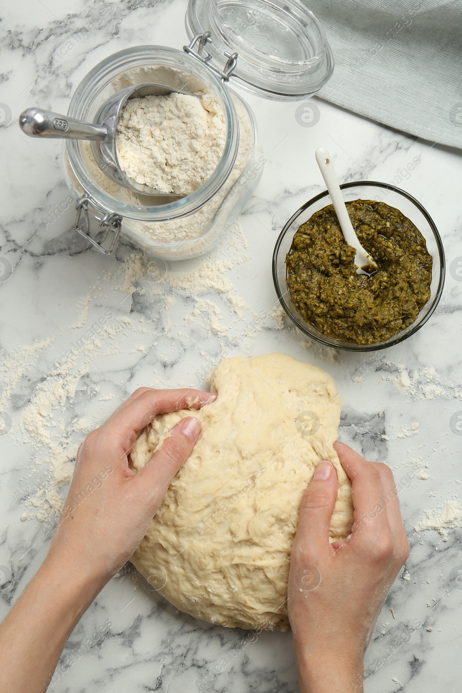 Photo of Woman kneading dough at white marble table, top view. Making delicious pesto bread