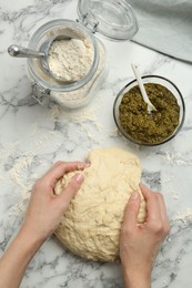 Woman kneading dough at white marble table, top view. Making delicious pesto bread