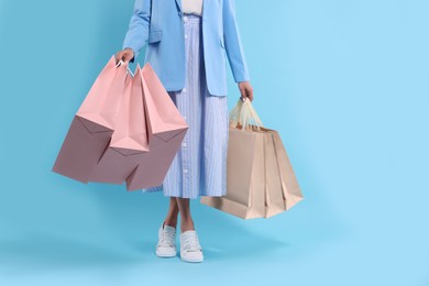 Woman with shopping bags on light blue background, closeup. Space for text