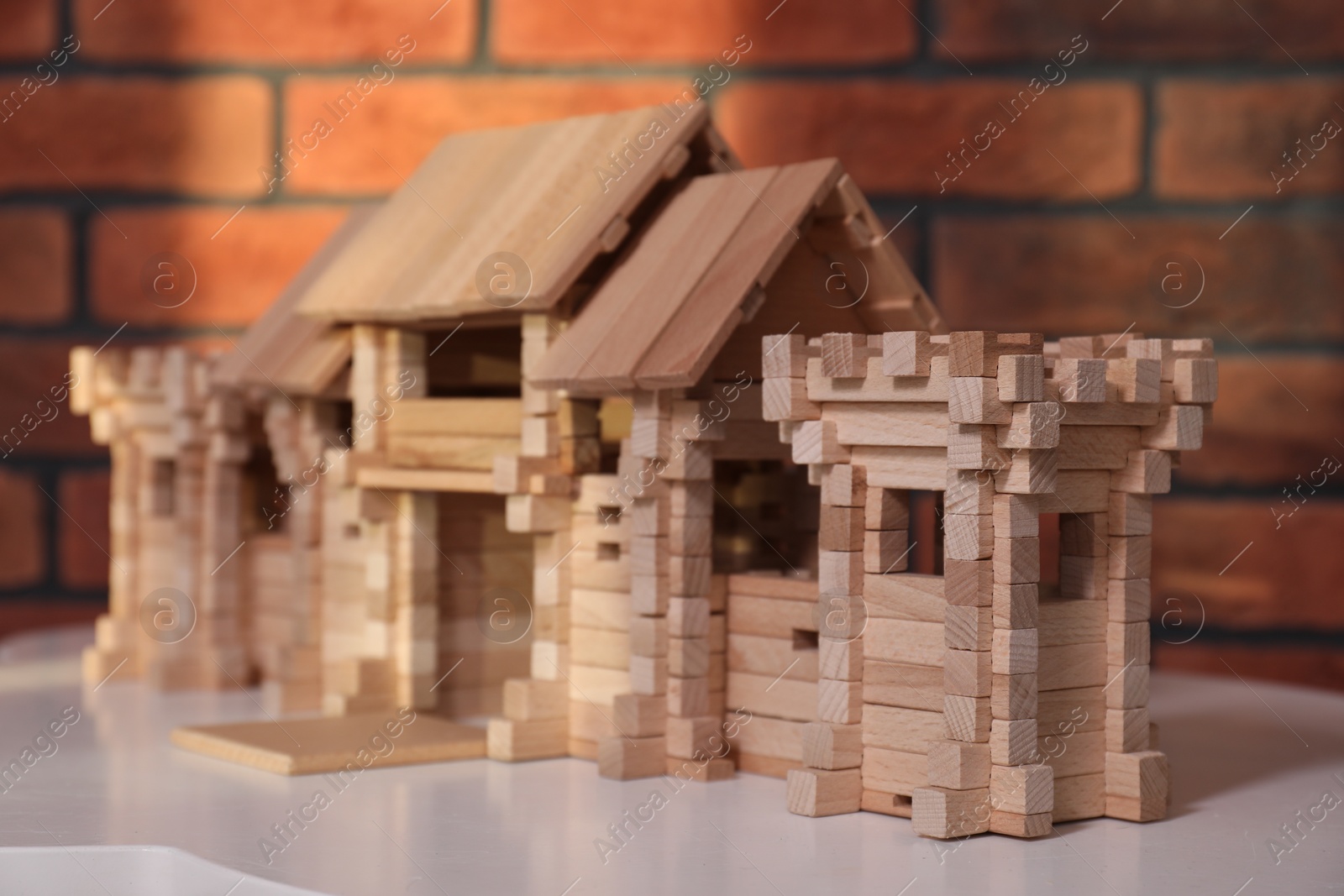 Photo of Wooden castle on white table near brick wall, closeup. Children's toy