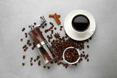 Photo of Manual coffee grinder with powder, beans and cup of drink on light grey table, flat lay
