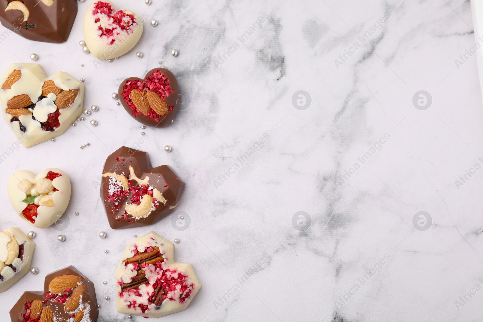 Photo of Tasty chocolate heart shaped candies with nuts on white marble table, flat lay. Space for text