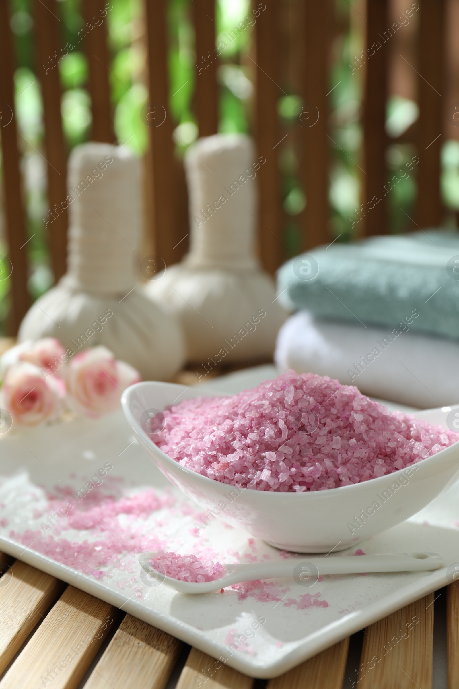 Photo of Bowl of pink sea salt on wooden table, closeup. Space for text