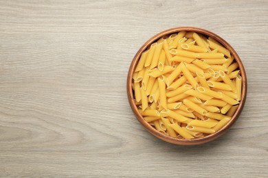 Raw penne pasta in bowl on light grey wooden table, top view. Space for text