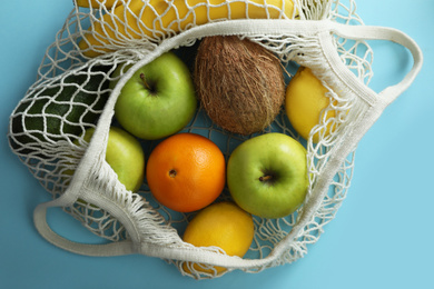 Net bag with fruits on light blue background, top view