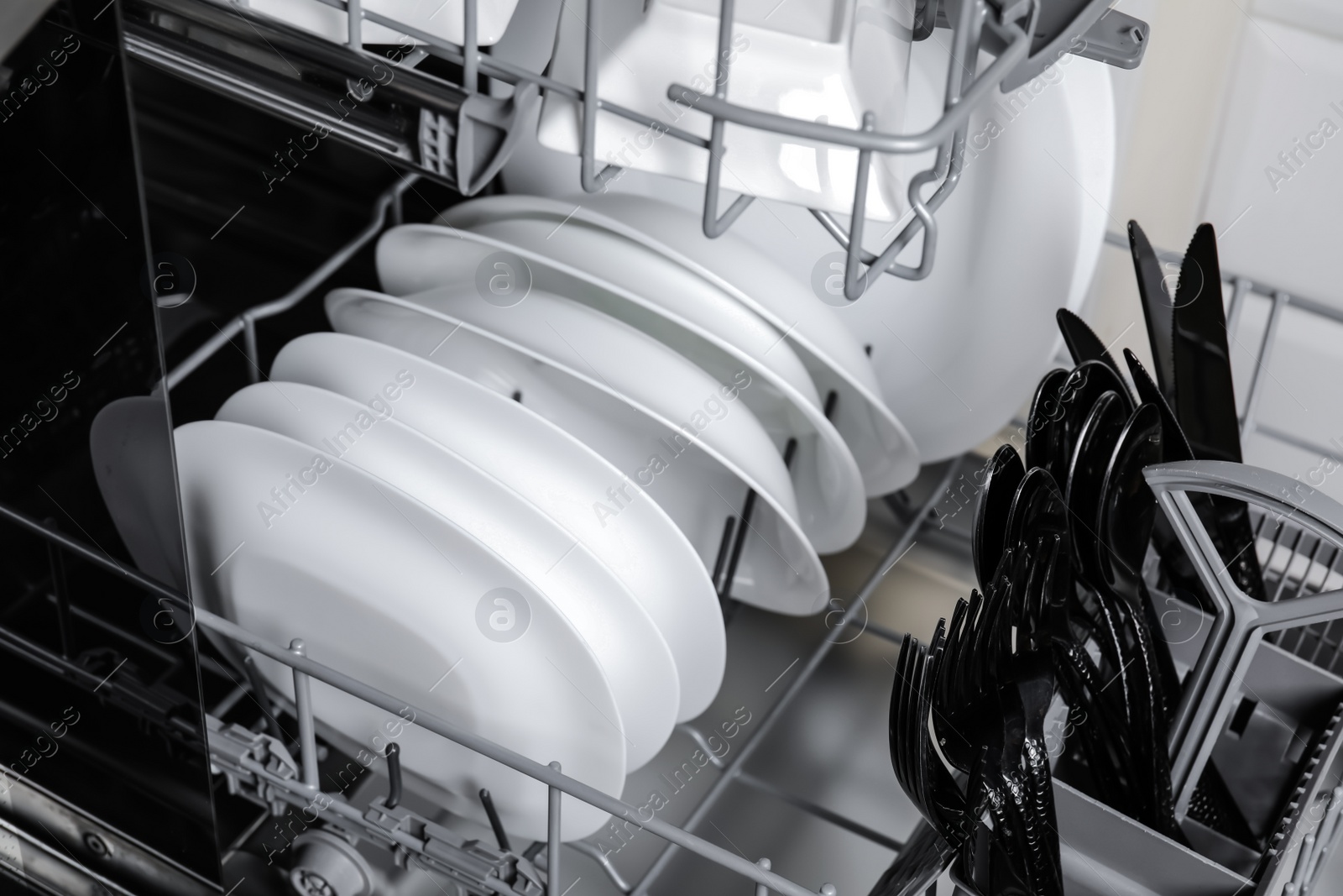 Photo of Open modern dishwasher with clean tableware, closeup