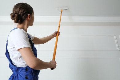 Photo of Worker painting ceiling with white dye indoors, back view. Space for text