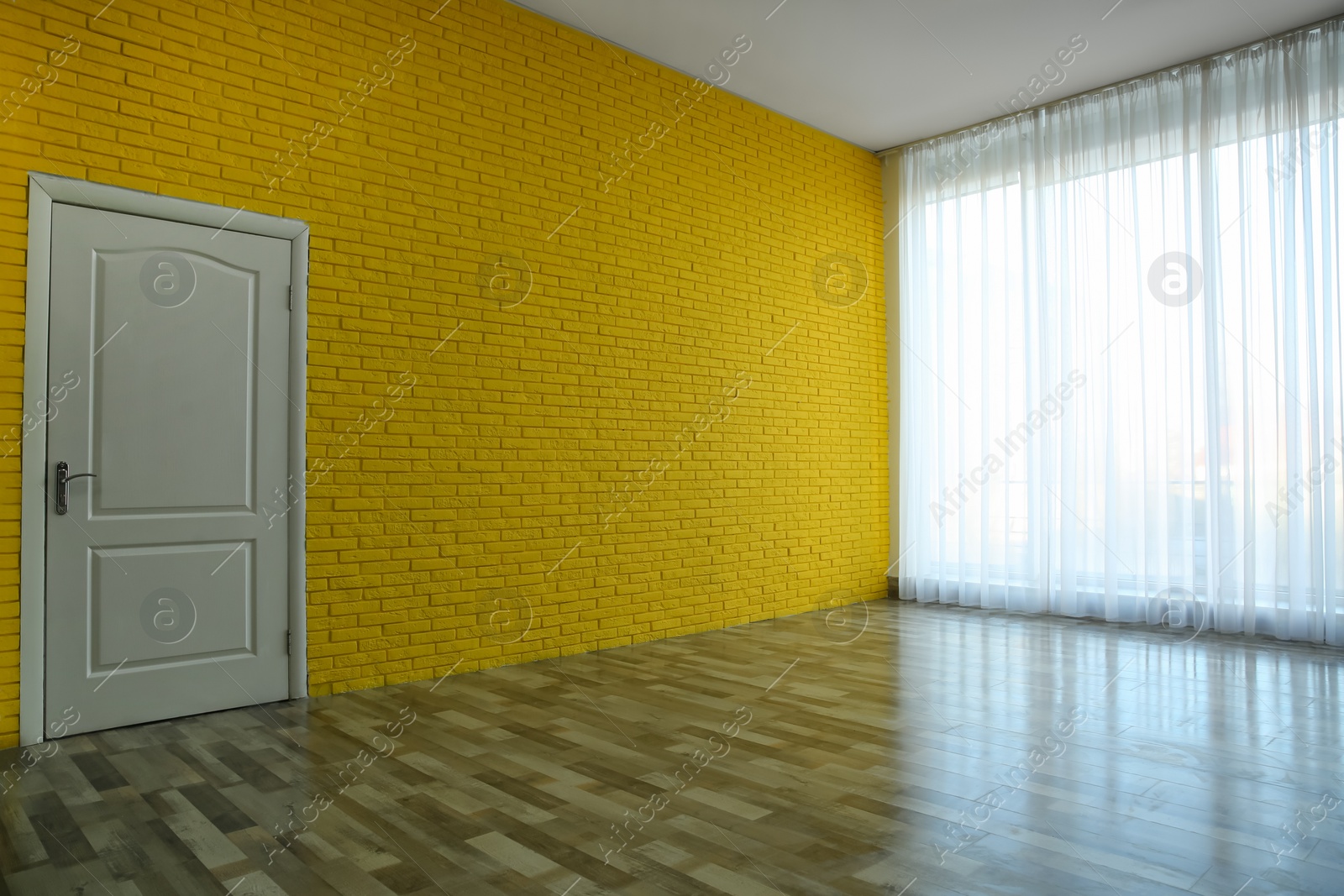 Photo of Empty room with yellow brick wall, large window and white door