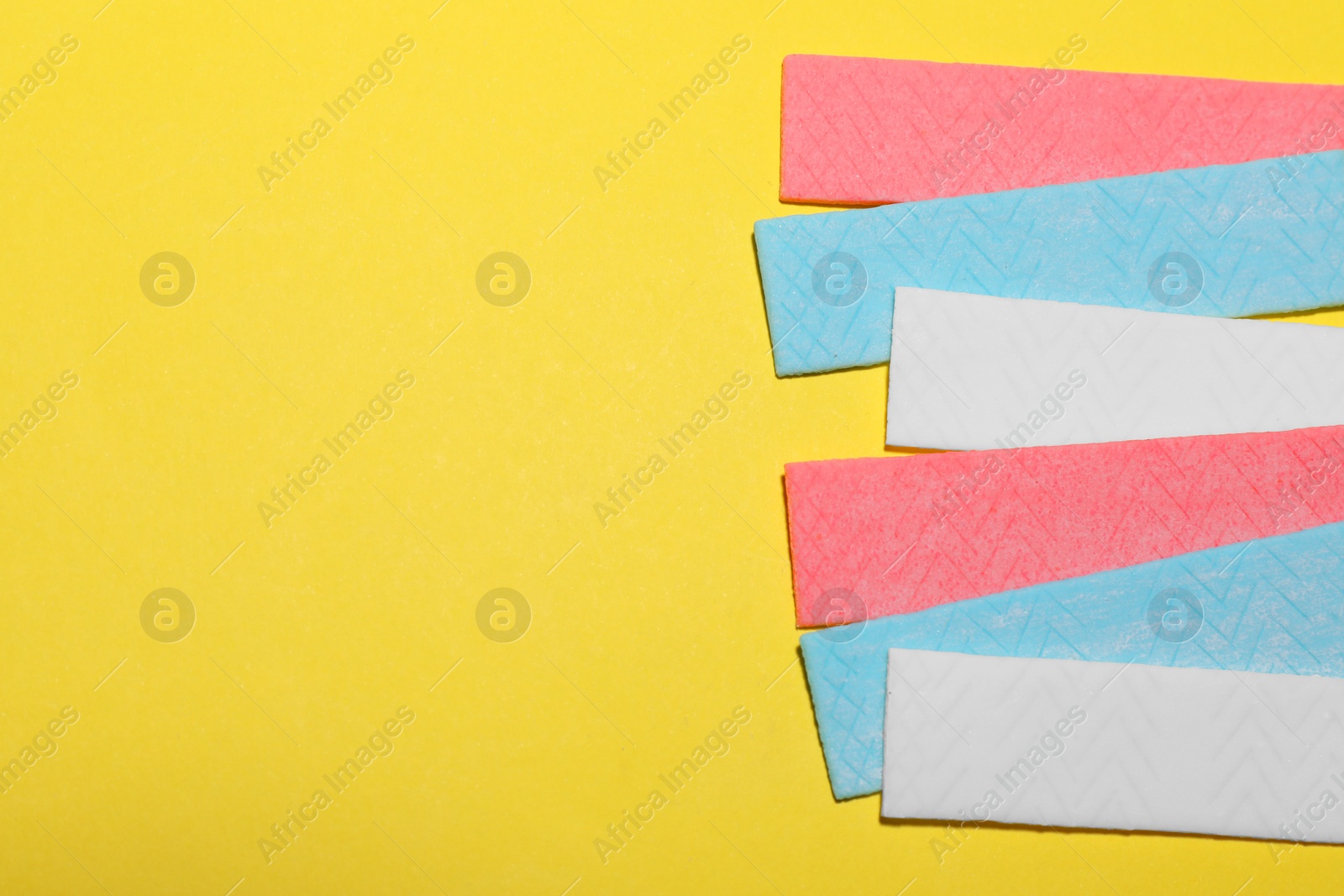 Photo of Sticks of tasty chewing gum on yellow background, flat lay. Space for text