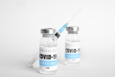 Photo of Vials with coronavirus vaccine and syringe on white background