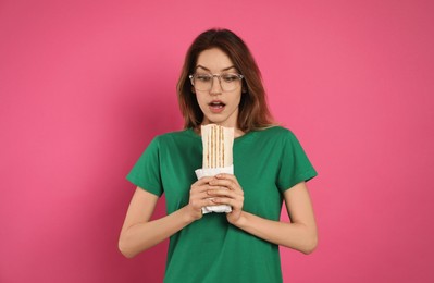 Emotional young woman with delicious shawarma on pink background