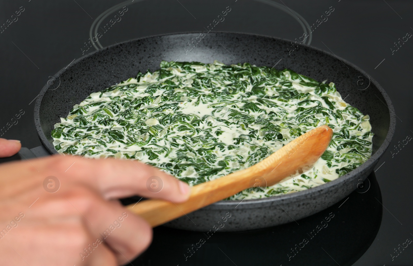 Photo of Woman cooking tasty spinach dip on kitchen stove, closeup view