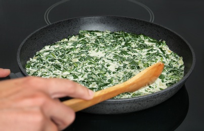 Photo of Woman cooking tasty spinach dip on kitchen stove, closeup view