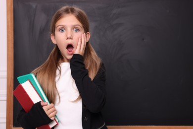 Photo of Shocked schoolgirl with books near blackboard. Space for text