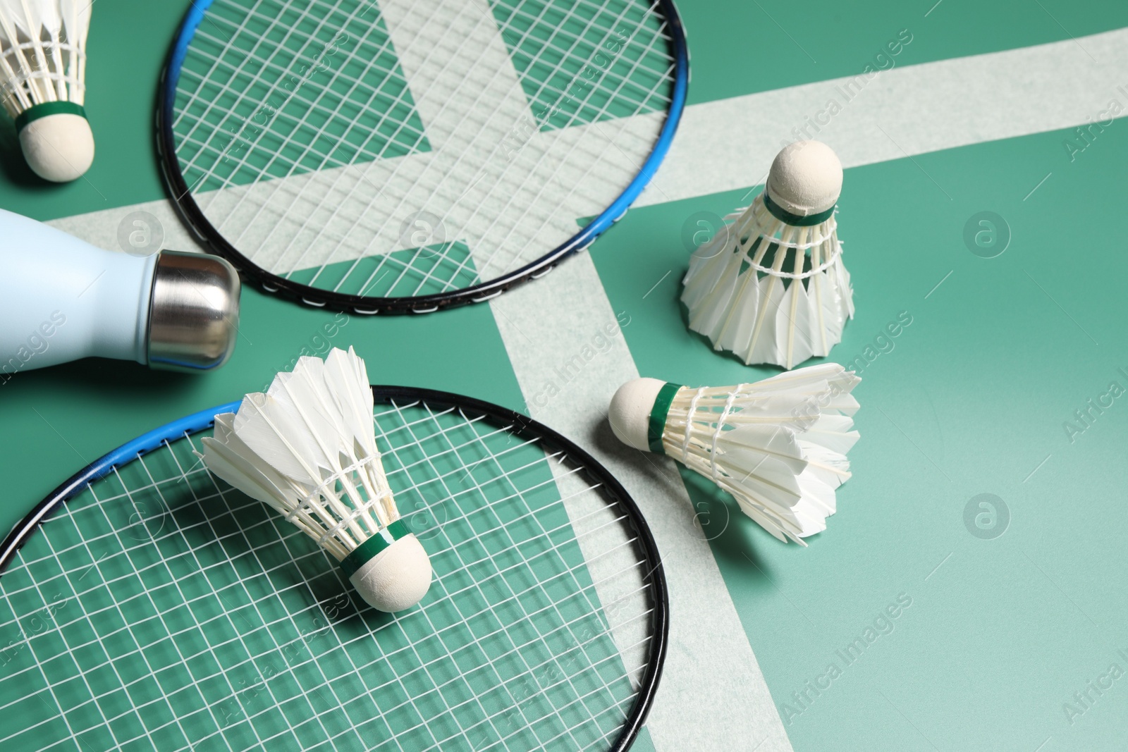 Photo of Feather badminton shuttlecocks, rackets and bottle on court