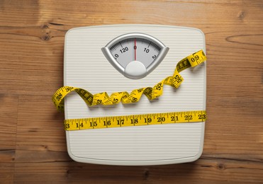Photo of Scales tied with measuring tape on wooden background, top view