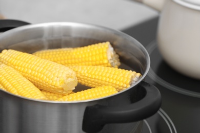 Photo of Stewpot with water and corn cobs on stove, closeup