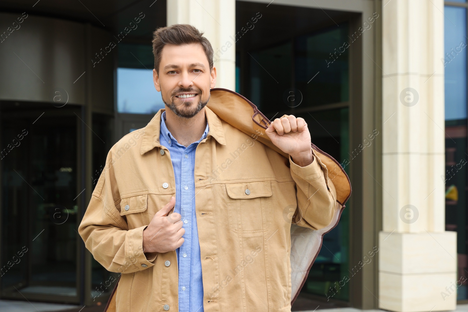 Photo of Attractive happy man holding garment cover with clothes outdoors. Dry cleaning service