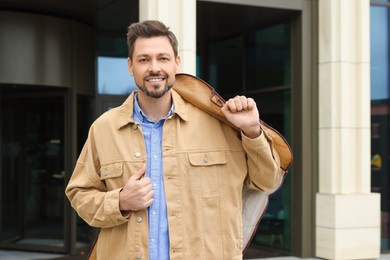Photo of Attractive happy man holding garment cover with clothes outdoors. Dry cleaning service
