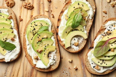 Photo of Delicious bruschettas with avocado on wooden table, flat lay