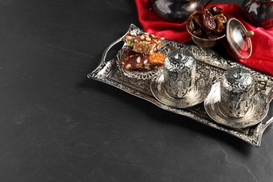 Photo of Tea, Turkish delight and date fruits served in vintage tea set on black table, space for text