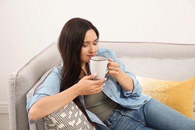 Photo of Young woman with cup of drink relaxing on couch at home