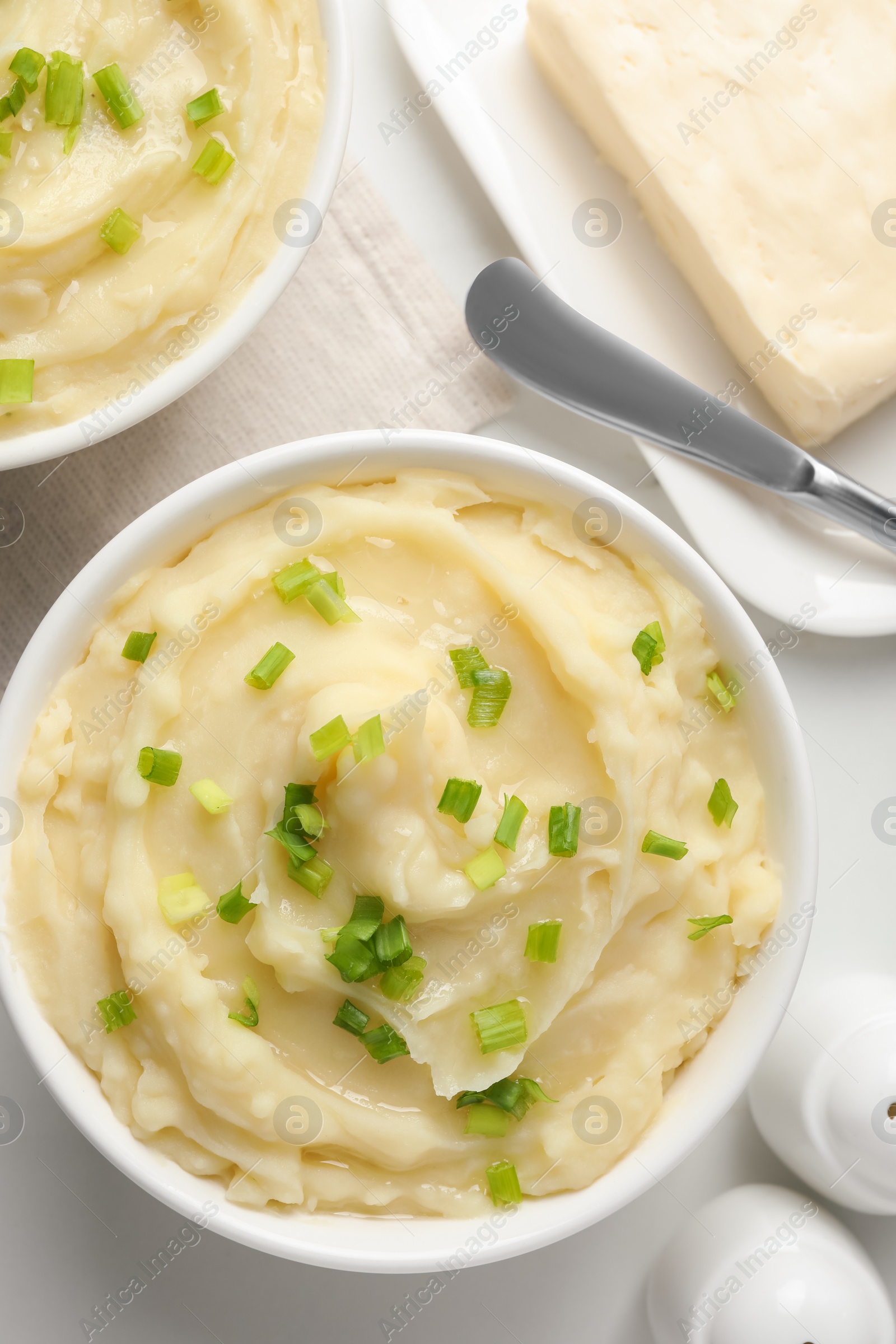 Photo of Bowls of delicious mashed potato with green onion on white table, flat lay