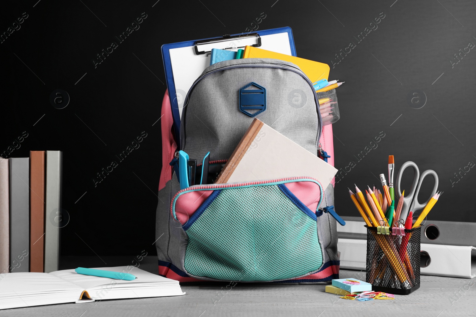 Photo of Backpack with different school stationery on grey wooden table near blackboard