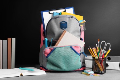 Photo of Backpack with different school stationery on grey wooden table near blackboard