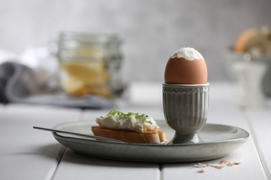 Photo of Fresh soft boiled egg in cup and sandwich on white wooden table. Space for text
