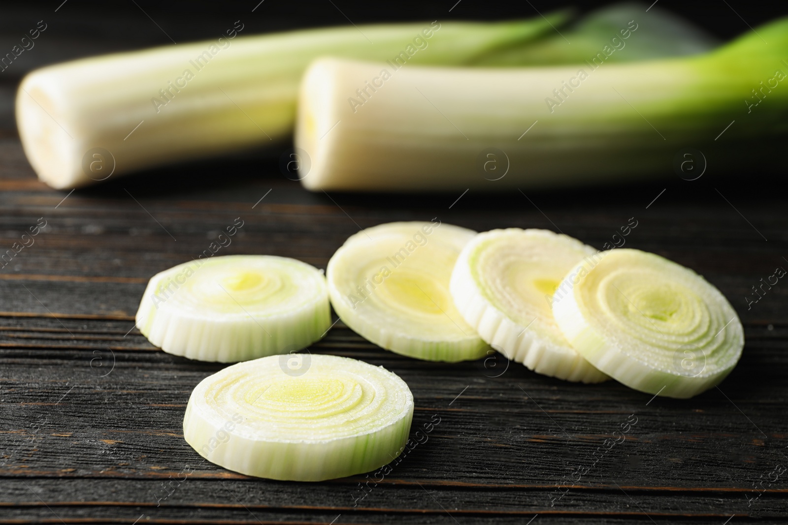 Photo of Fresh raw leek on black wooden table, closeup. Ripe onion