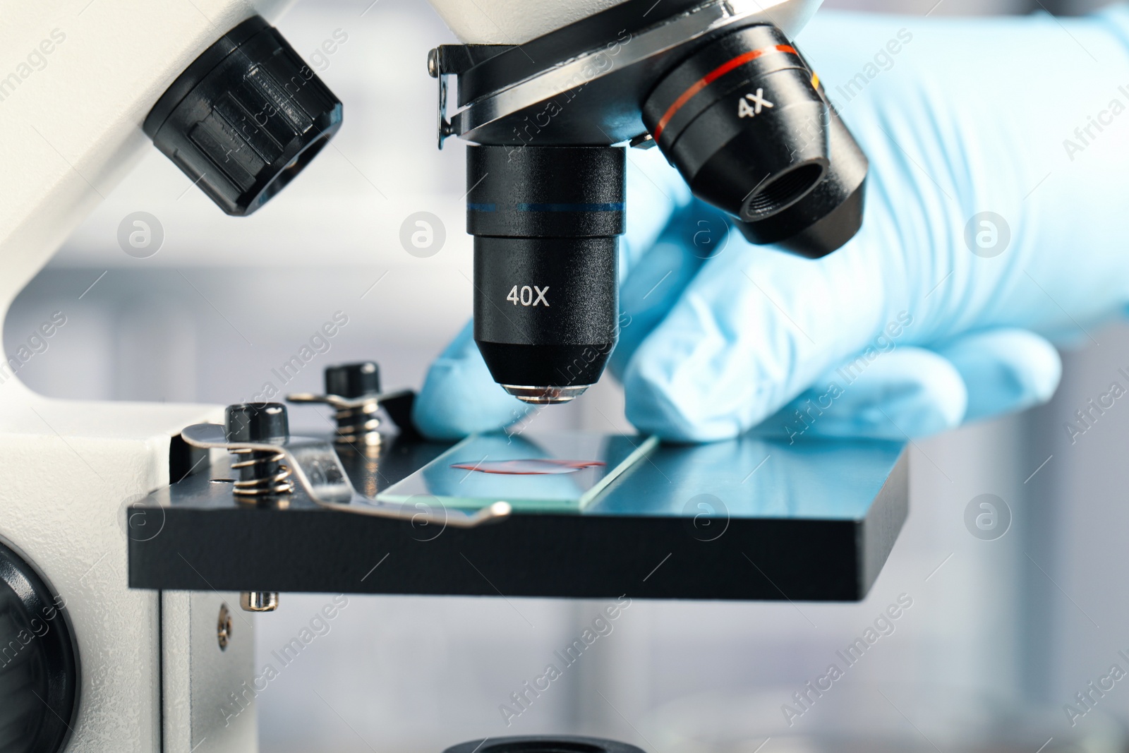 Photo of Scientist examining sample of red liquid on slide under microscope in laboratory, closeup